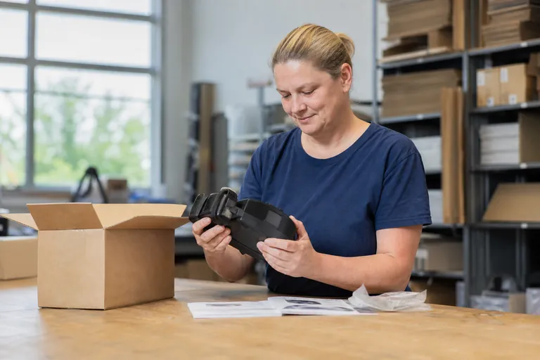 Händlerin prüft ein batteriebetriebenes Kleingerät neben Versandkarton und Unterlagen